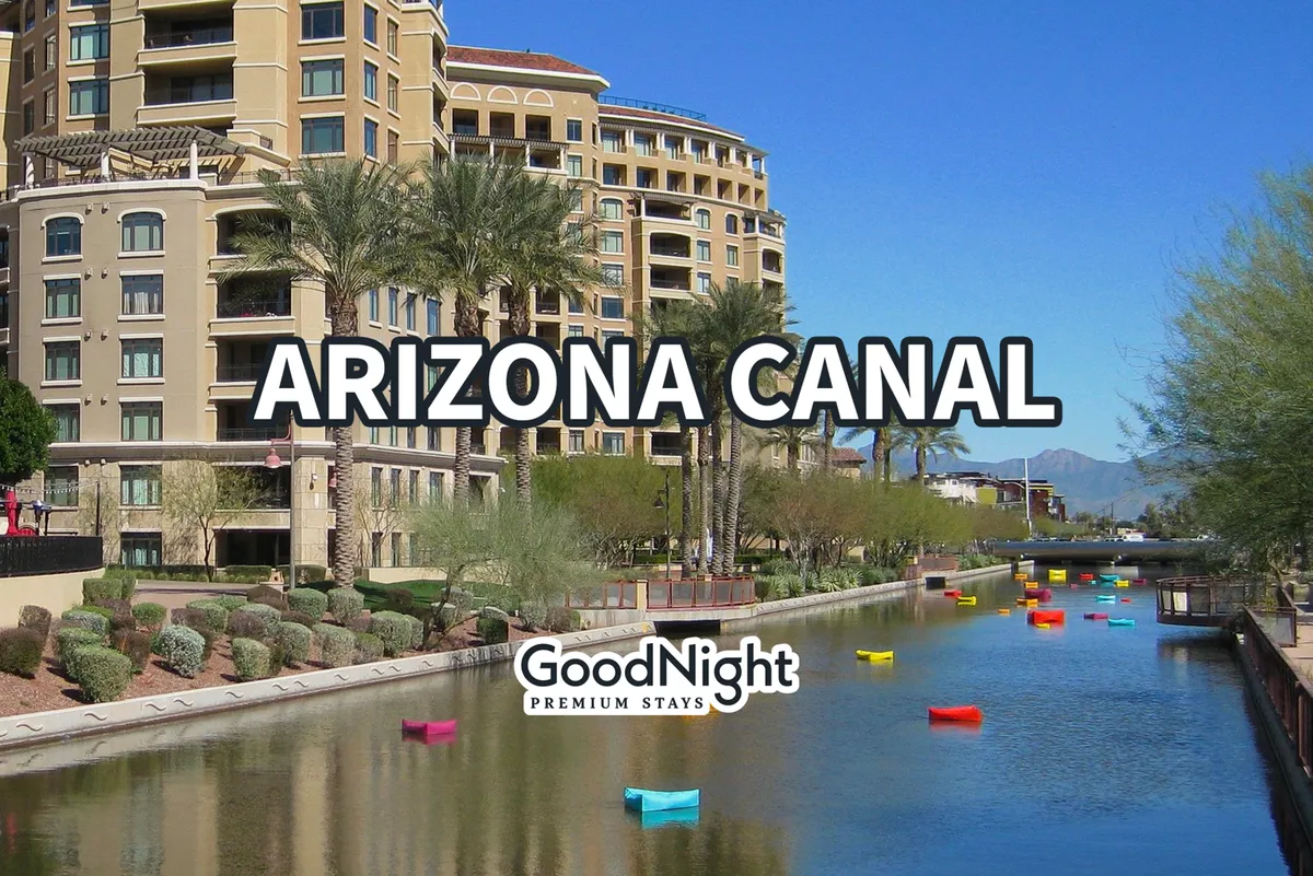 A picturesque view of the Arizona Canal bordered by palm trees and modern apartment buildings. Colorful boats dot the calm canal, and the vibrant setting suggests a lively area for walking, exploring, and enjoying local culture.
