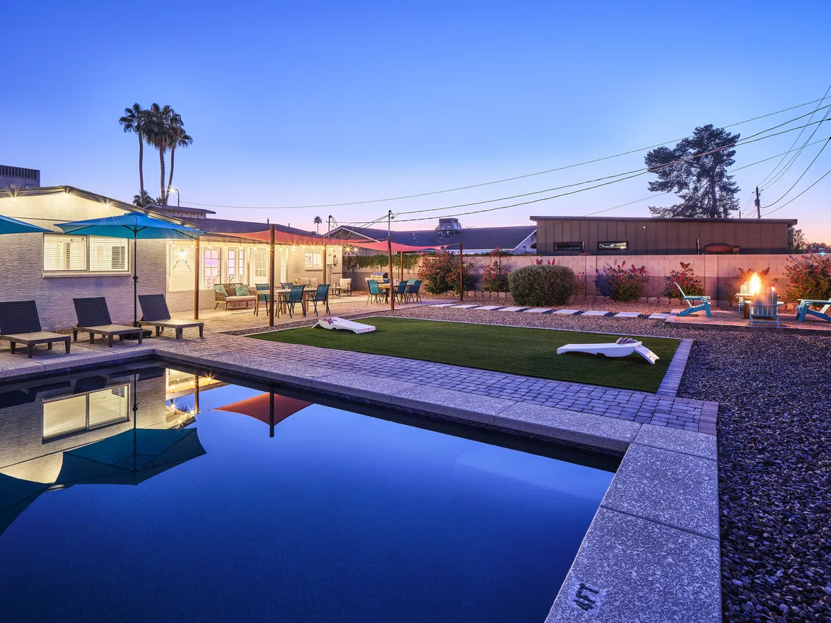 The image showcases a stunning Scottsdale backyard with a sparkling private pool surrounded by inviting lounge chairs, a cozy fire pit for evening gatherings, and an al fresco dining area perfect for entertaining. The scene captures a tranquil yet social atmosphere, highlighting the outdoor living spaces ideal for relaxation and connection.