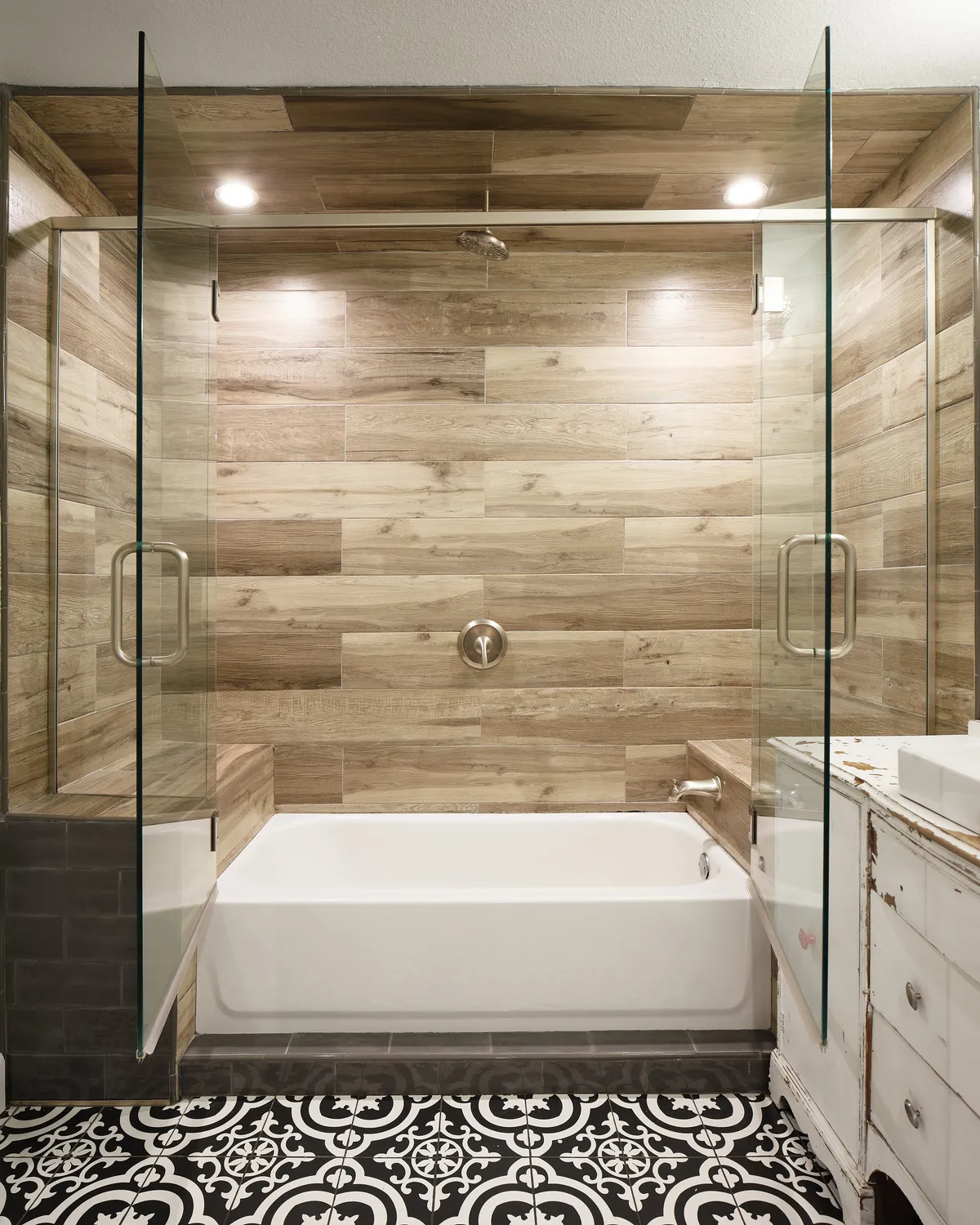 The bathroom features a glass shower enclosure, a freestanding bathtub, and eye-catching patterned floor tiles. The design is modern and calm, suggesting a spa-like experience and attention to detail in amenities, mirroring a boutique hotel's thoughtful touches.