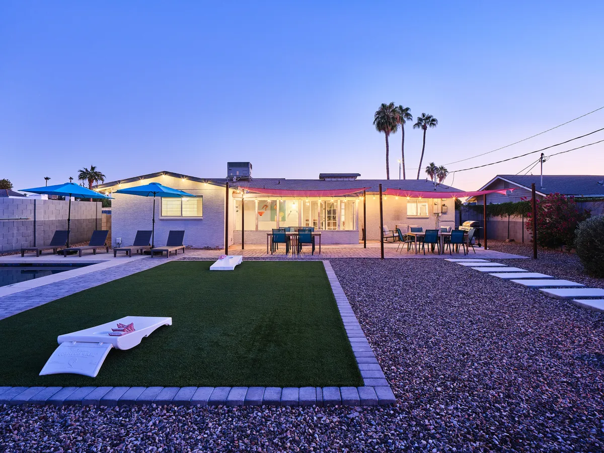 This image features a sparkling swimming pool surrounded by poolside loungers and colorful umbrellas, with palm trees framing the area. There is an outdoor seating and dining area nearby, all set under a cheerful Arizona sky. In the background, the sunset hints at evening activities and relaxation.