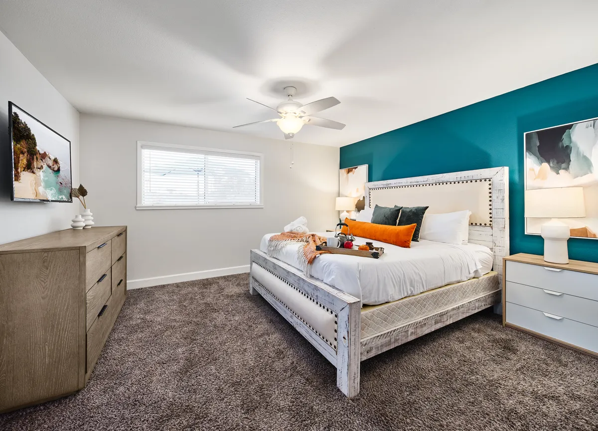 A serene bedroom featuring a comfortable bed with plush bedding, a nightstand with a lamp, a dresser, stylish artwork, and a window that allows natural light to fill the space. The overall decor is calm and cozy, perfect for restful nights after a day of adventure.