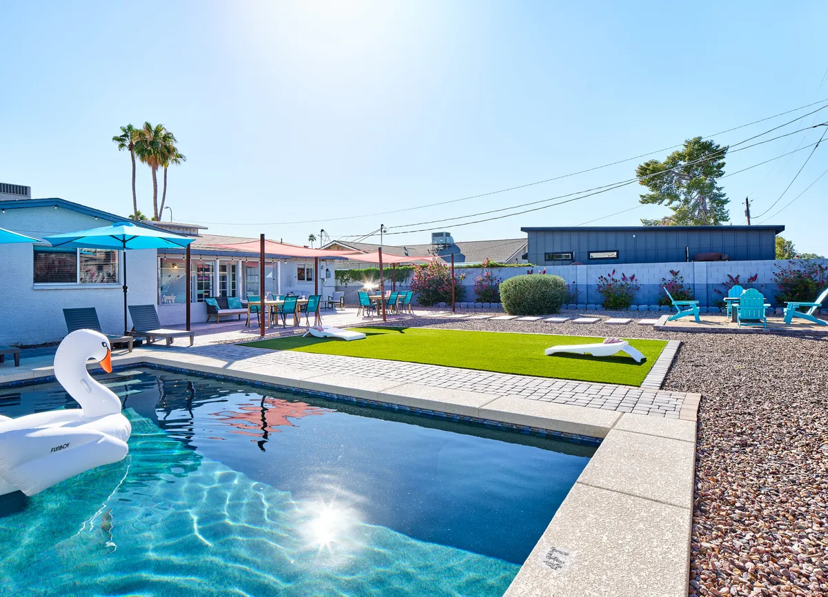 A sunlit backyard featuring a sparkling swimming pool with a whimsical swan float, lawn area, lounge chairs, and umbrellas. The playful setup hints at lively pool parties, relaxation, and outdoor games—an ideal private space for families to unwind and enjoy each other's company.