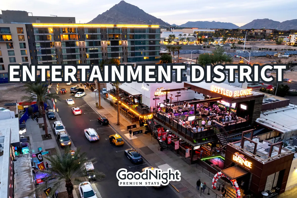 This vibrant exterior image captures the bustling heart of Scottsdale’s Entertainment District, with prominent signage, the lively Bottled Blonde venue, colorful vehicles, and palm trees all set against a stunning mountain sunset backdrop. The scene is filled with energy, suggesting the district’s array of nightlife options and social experiences.